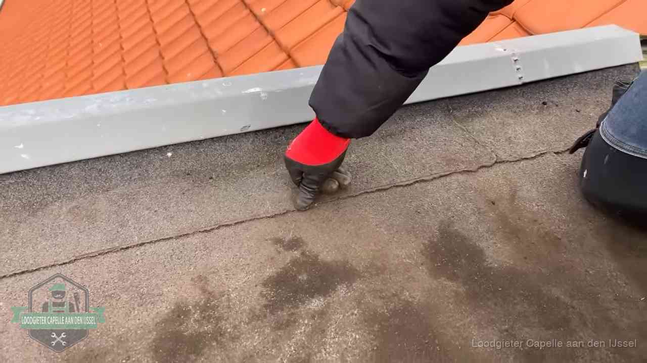 Vakman wijst een naad met vochtplekken aan op een bitumen plat dak in Capelle aan den IJssel