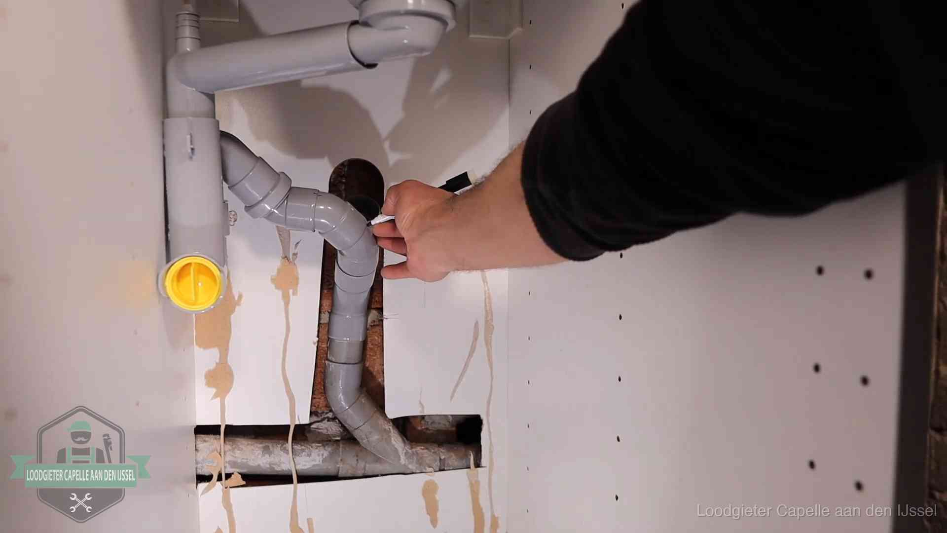 Loodgieter voor verhuurders en bedrijven in Capelle aan den IJssel Loodgieter markeert een pvc-afvoerbuis onder een gootsteen in Capelle aan den IJssel