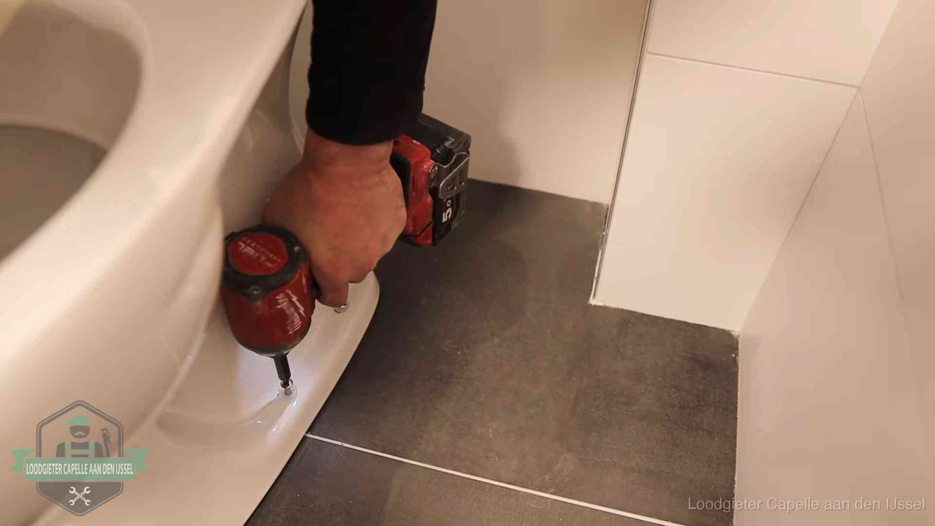 Loodgieter zet de voet van een wc-pot vast op de tegelvloer in Capelle aan den IJssel